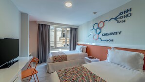 Une chambre d’hôtel avec deux lits, un bureau avec une télévision, une chaise et une fenêtre avec des rideaux.