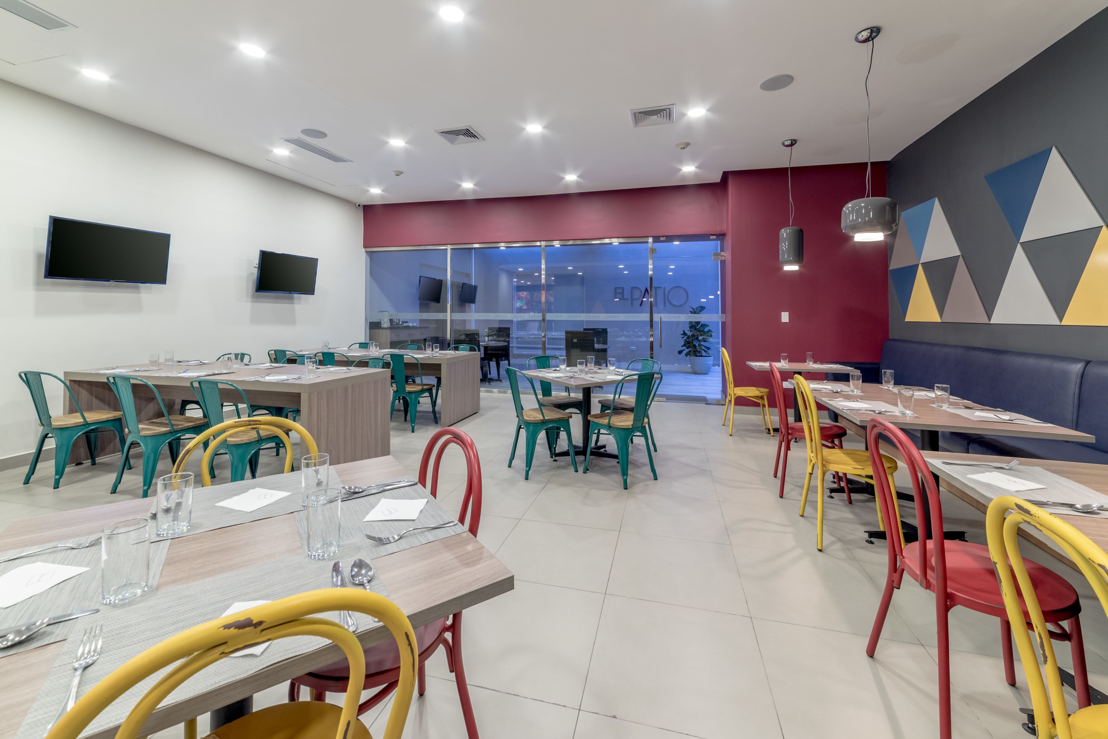 Een modern restaurant met meerdere tafels en stoelen, een groot televisiescherm en een glazen wand met uitzicht op het interieur.
