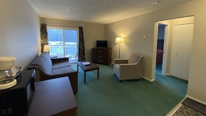 Habitación de hotel con sofá, sillón, televisión de pantalla plana, lámpara y vistas al exterior.