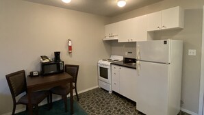 Una cocina funcional con armarios blancos, un refrigerador, una estufa y un microondas. Hay una mesa de comedor con sillas y un extintor de incendios montado en la pared.