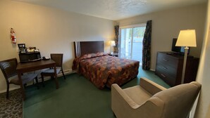 Una habitación de hotel con cama, escritorio con microondas, silla, cómoda y televisión.