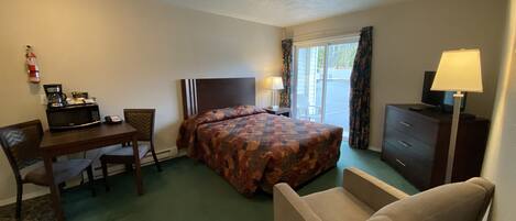 Ein Hotelzimmer mit einem Bett, einem Schreibtisch mit eingebauter Mikrowelle, einem Sessel, einem Schminktisch und einem Fernseher.