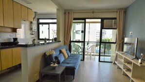 A modern apartment with a kitchen, a living area with a sofa and TV, and a balcony with chairs. - Barrabella Pé na areia (Rio de Janeiro)