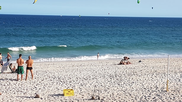 A beach with people, a yellow box labeled "SKOL", and a clear blue sky. - Barrabella Pé na areia (Rio de Janeiro)