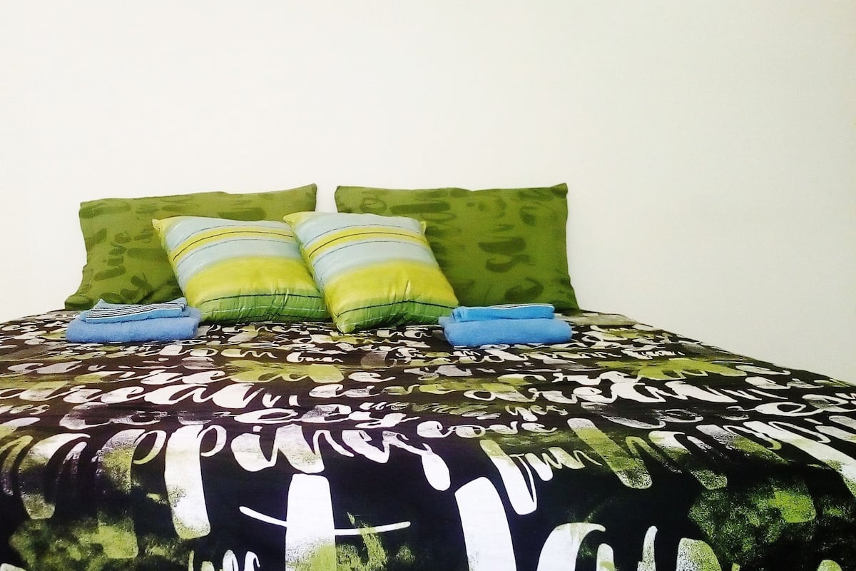 Una cama con una colcha estampada, dos almohadas verdes y dos toallas azules dobladas.
