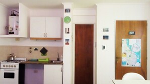 A compact kitchen with white cabinets, a gas stove, a sink, and a wooden door. - Isla Verde (Rosario)