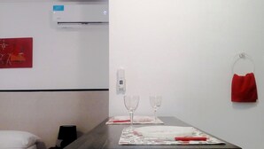 Habitación de hotel con cama, una mesa con dos copas de vino, una toalla roja y un aire acondicionado de pared.