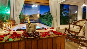 Quarto com uma janela grande, uma mesa de madeira, uma garrafa de champanhe, um balde e um prato de uvas.