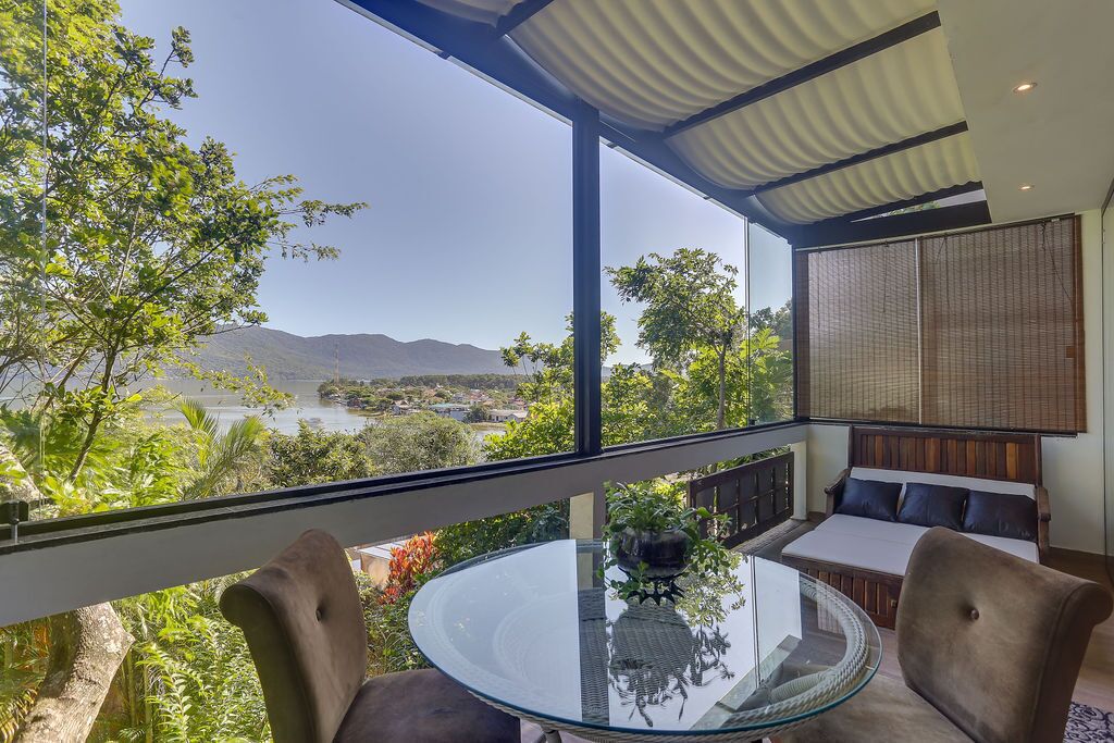 A modern room with a glass table and chairs, a sofa, and a view of a lake and mountains.