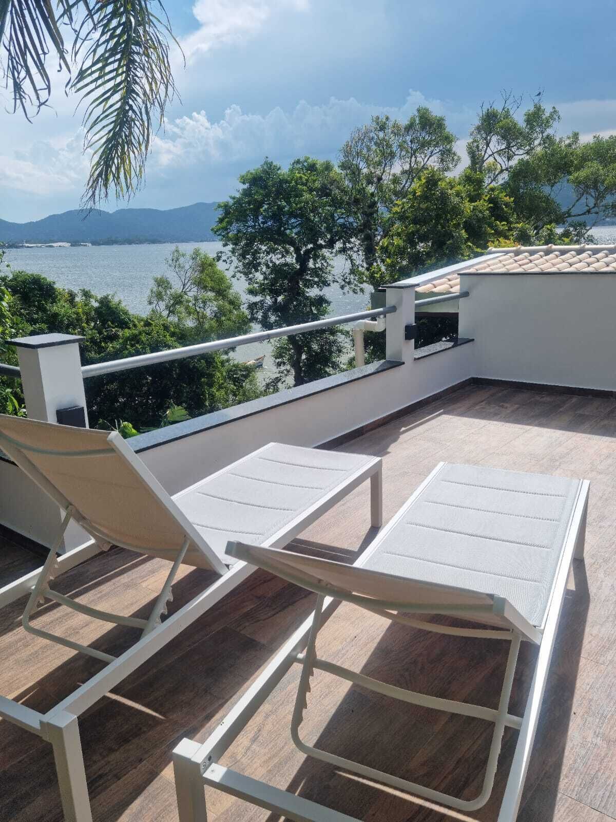 Terraza en la azotea con dos sillones blancos y una mesa, con vistas a un cuerpo de agua y vegetación.