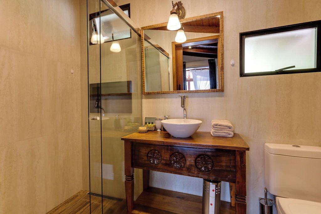 Un bagno con cabina doccia in vetro, mobile lavabo in legno con lavandino bianco e un water.