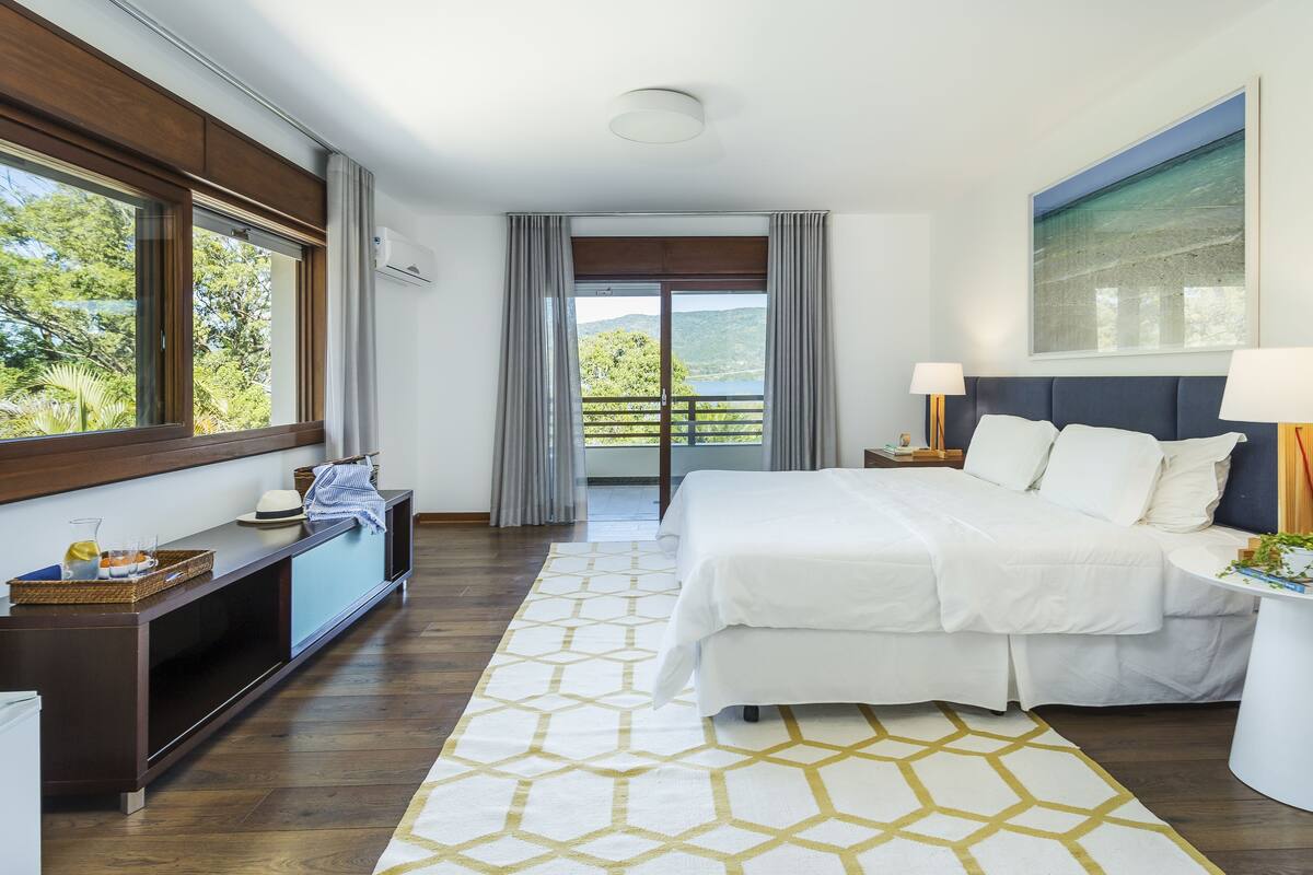 A modern hotel room with a large bed, a desk with a lamp, a view of the outdoors, and a balcony.