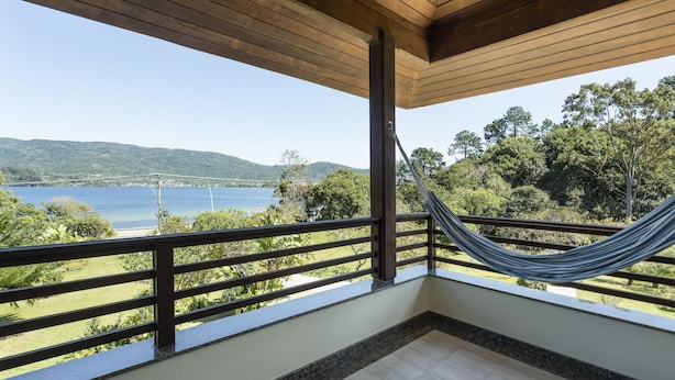 A balcony with a hammock, a view of a lake, and surrounding greenery. - Haute Haus (Florianópolis)