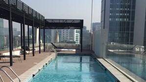 Una piscina sul tetto con acqua cristallina, circondata da lettini e un pergolato.
