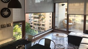 Un soggiorno moderno con un'ampia finestra, un'area pranzo e un balcone con mobili in vimini.