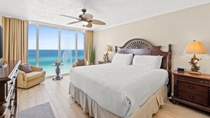 A spacious bedroom with a large bed, a ceiling fan, a nightstand with a lamp, and a view of the ocean through large windows. - Long Beach Resort by Panhandle Getaways (Panama City Beach)