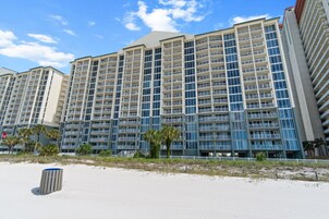 A multi-story hotel with balconies, located near a sandy beach.