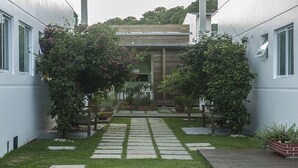 Un sendero estrecho que conduce a un edificio moderno con una terraza de madera y plantas en macetas.