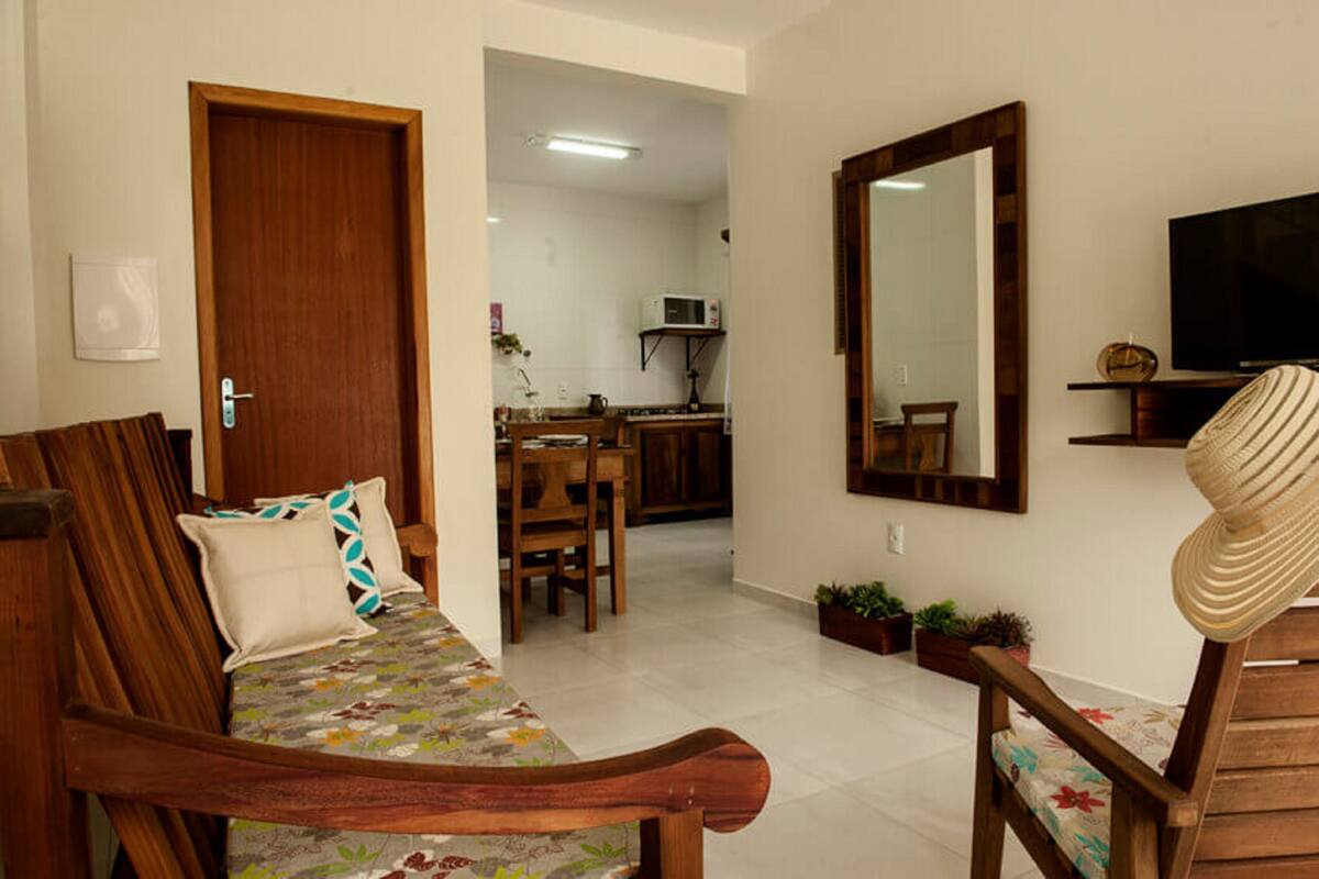 A living room with a sofa, a wooden chair, a dining table, and a kitchen in the background.