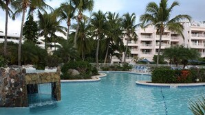 En swimmingpool med et vandfald, omgivet af palmer og en hotelbygning i baggrunden.