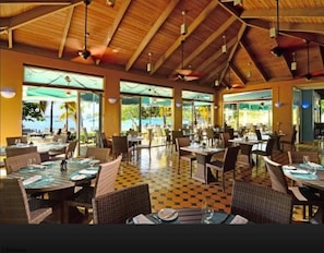 A spacious indoor dining area with high ceilings and large windows, featuring checkered flooring and wicker furniture.
