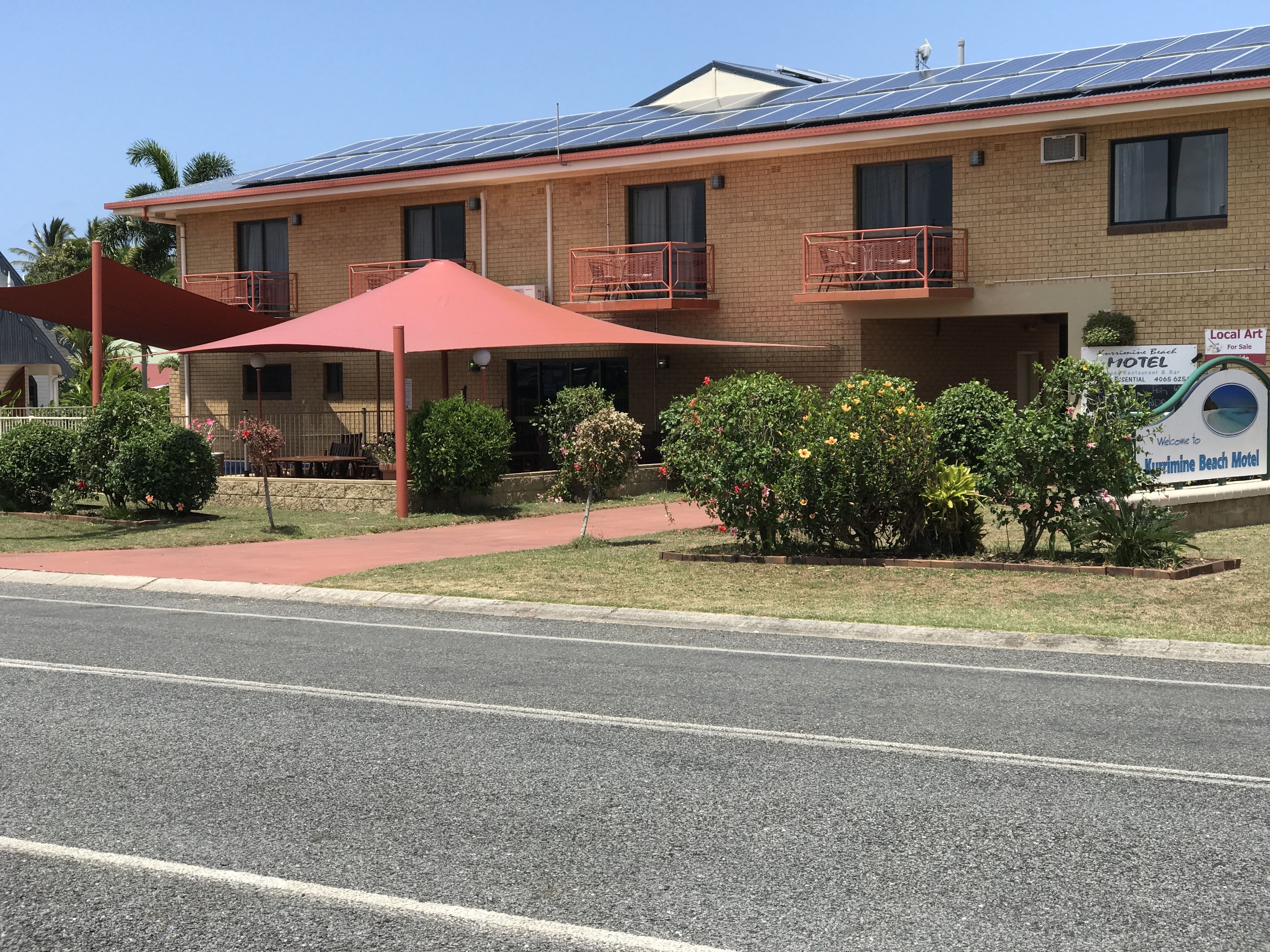 A motel with a brick facade, solar panels on the roof, and a sign advertising local art for sale.