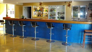 A bar area with blue-tiled walls, a counter with bottles, and four bar stools. - Kurrmine Beach Motel (Kurrimine Beach)