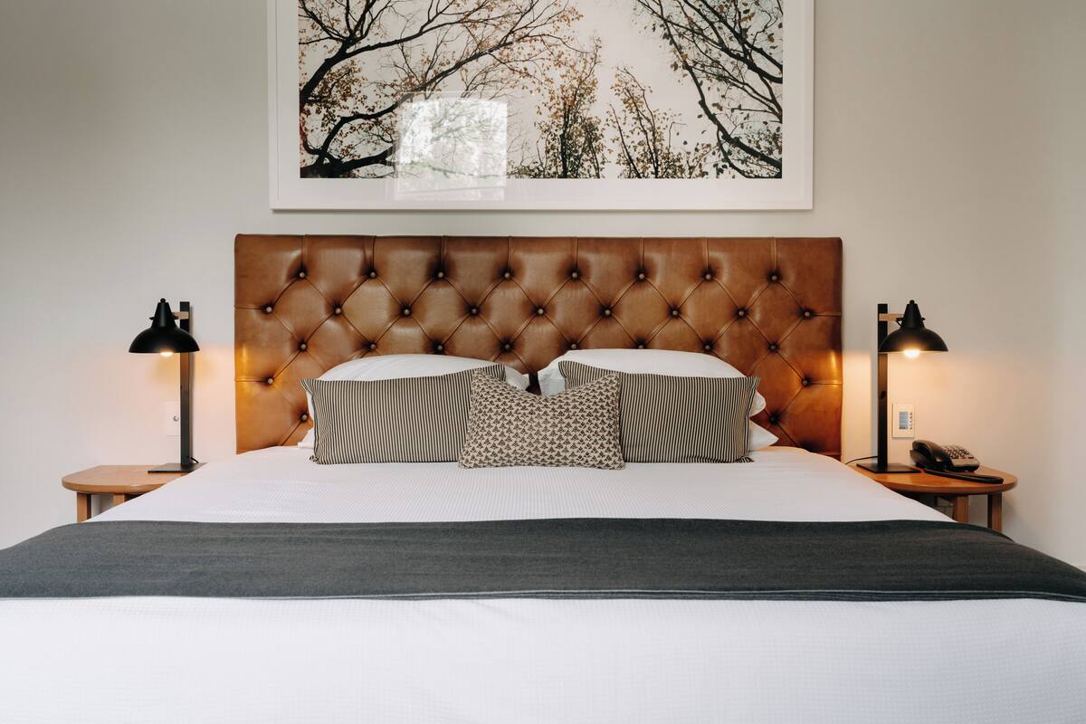 A neatly made bed with a tufted headboard, two bedside lamps, and a framed picture on the wall.
