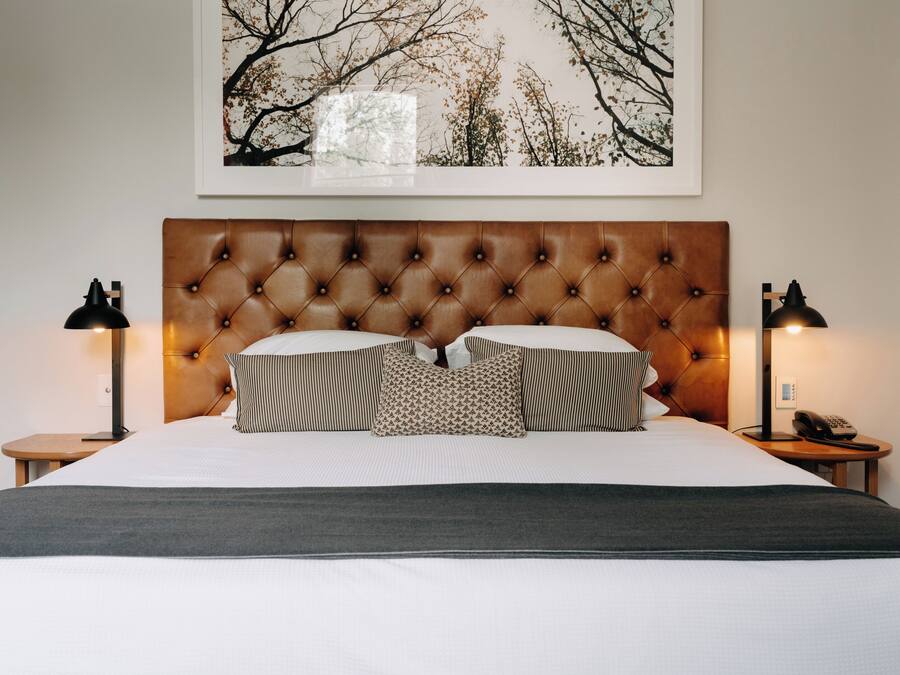 A neatly made bed with a tufted headboard, two bedside lamps, and a framed picture on the wall.