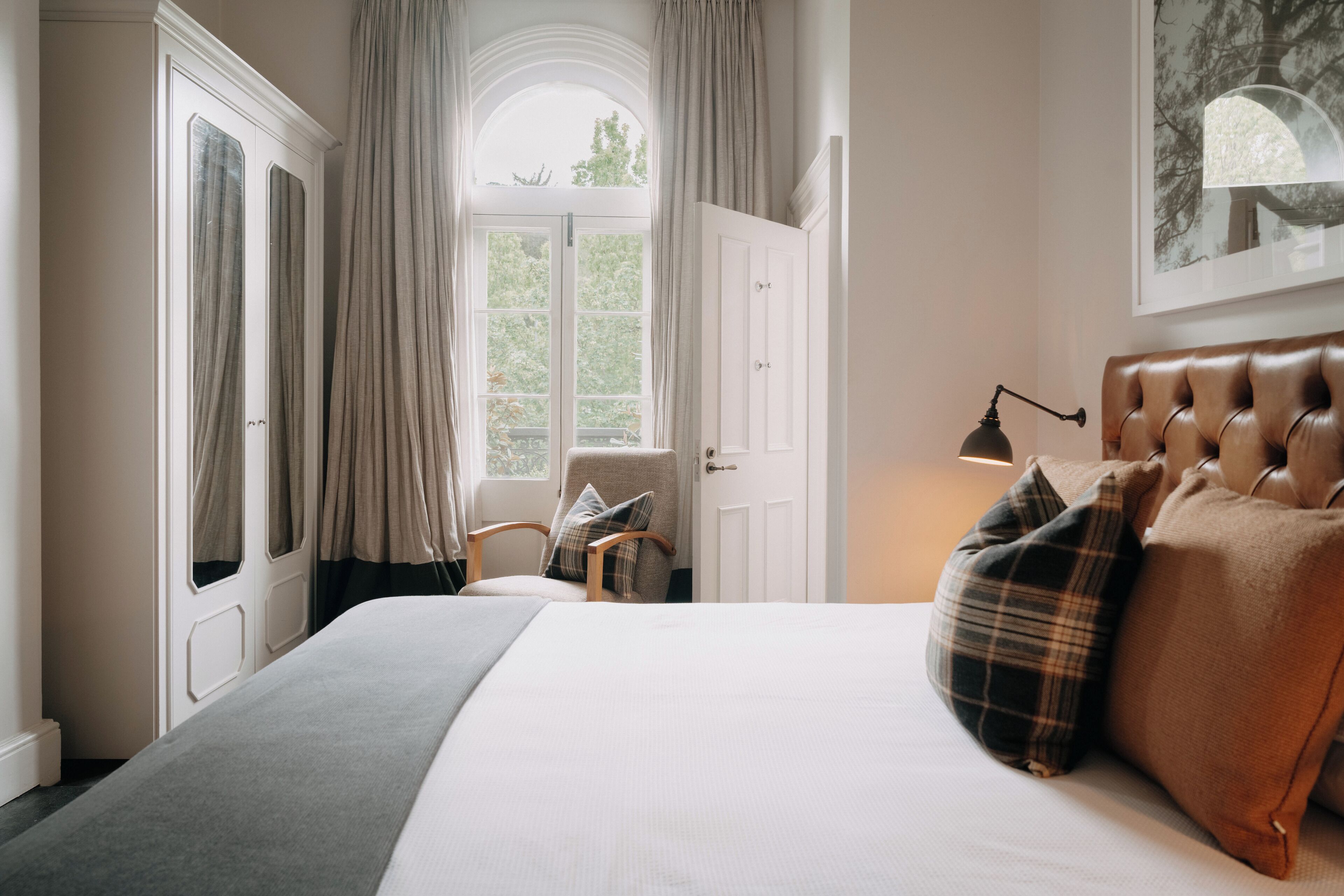 Une chambre à coucher avec un grand lit, une chaise, une armoire et une fenêtre avec des rideaux.