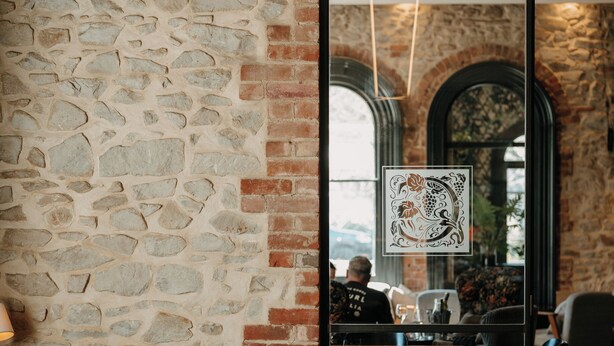 Un restaurante con paredes de piedra y detalles en ladrillo, con mesas redondas, copas de vino y menús.