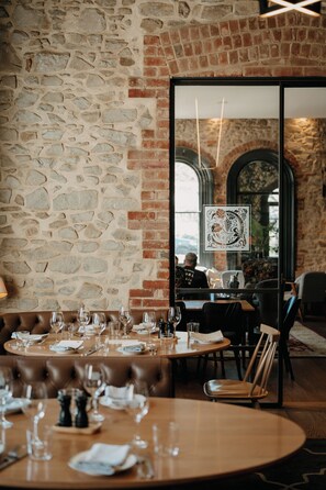 Un restaurante con paredes de piedra y detalles en ladrillo, con mesas redondas, copas de vino y menús.