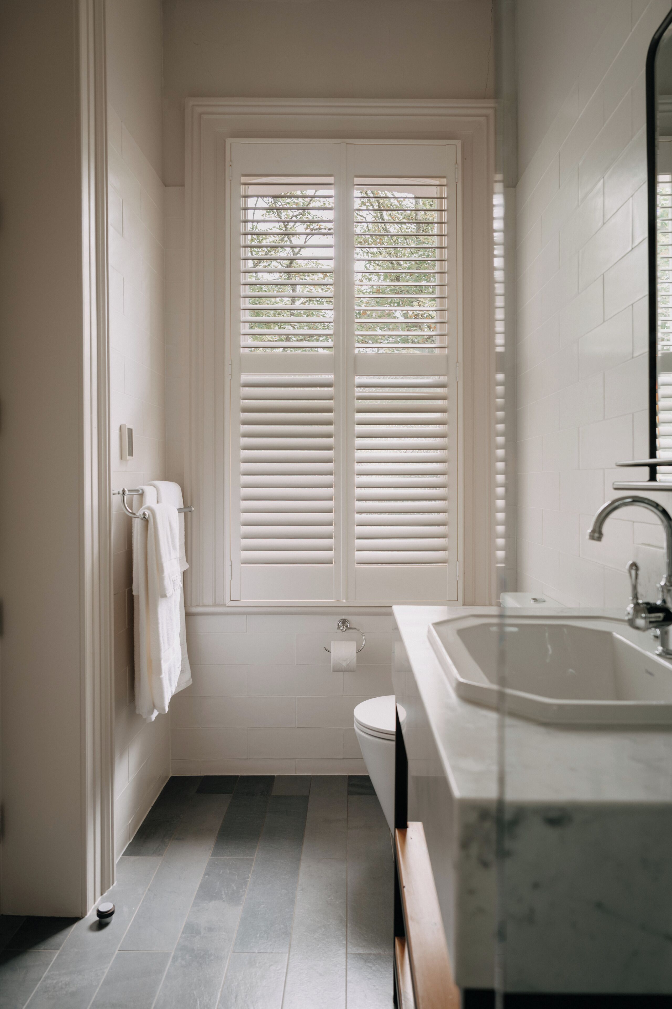 A bathroom with a white bathtub, a sink with a mirror, and a window with blinds.