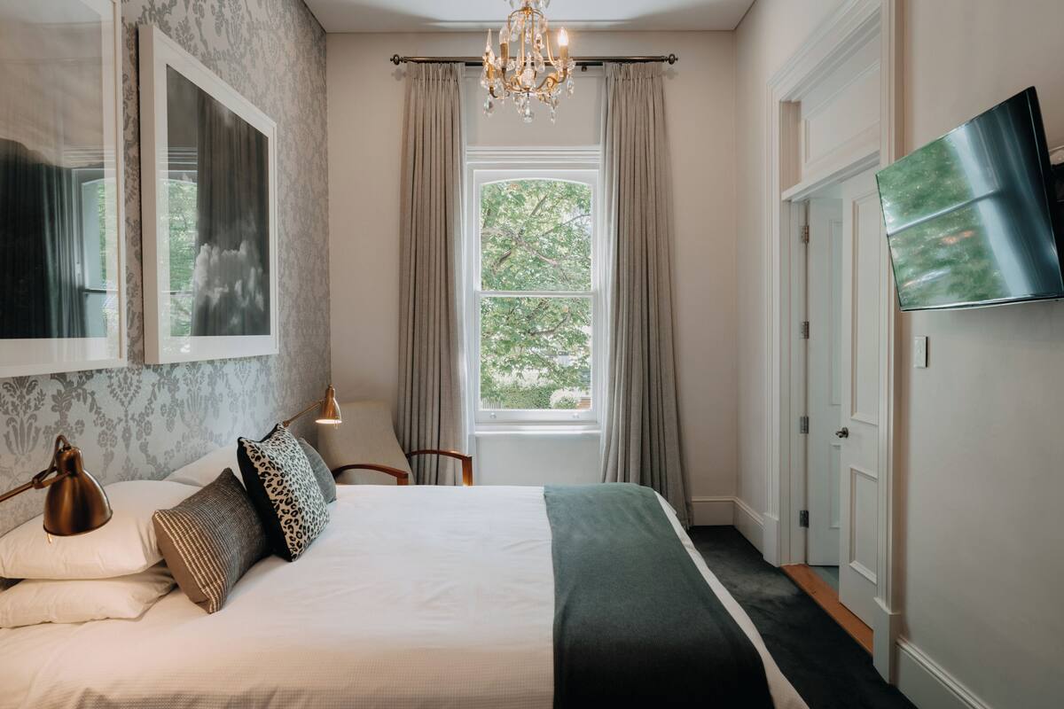 A bedroom with a bed, a chandelier, a TV, and a window with curtains.