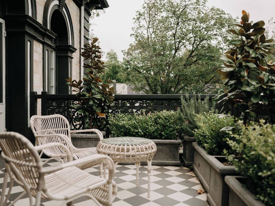 A checkered outdoor patio with wicker furniture and a view of trees and a building in the background.