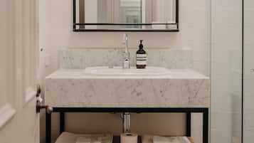 Un baño con lavamanos de mármol, espejo con marco negro y estante de madera con toallas.