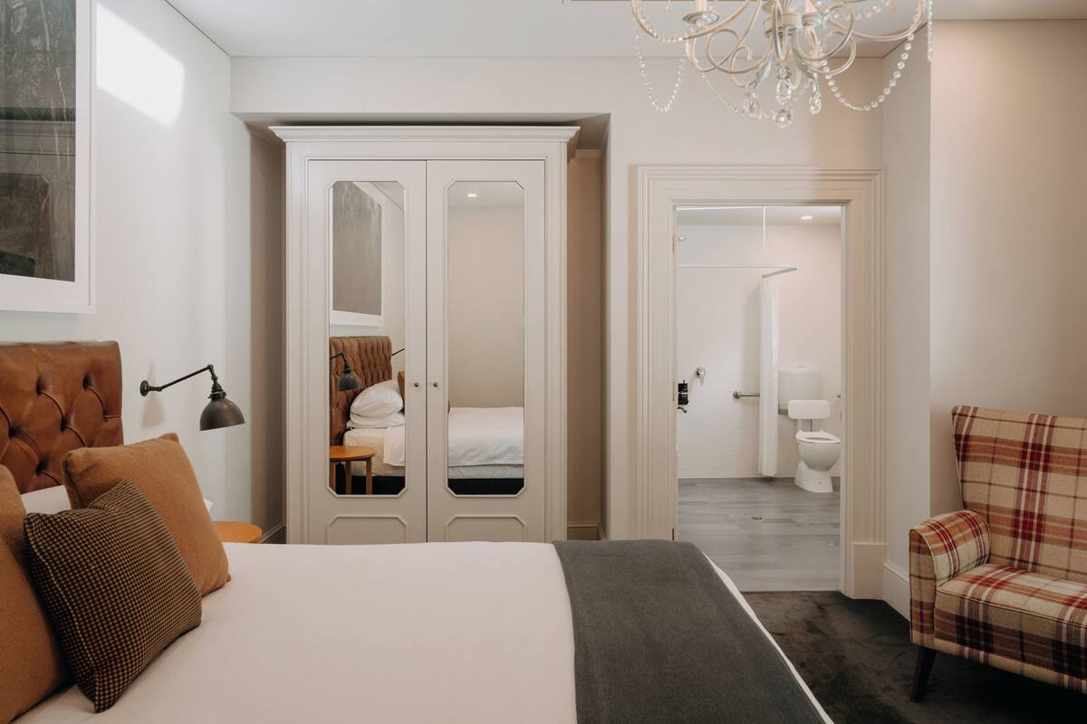 A bedroom with a bed, a wardrobe, a chair, and a bathroom visible through an open door.