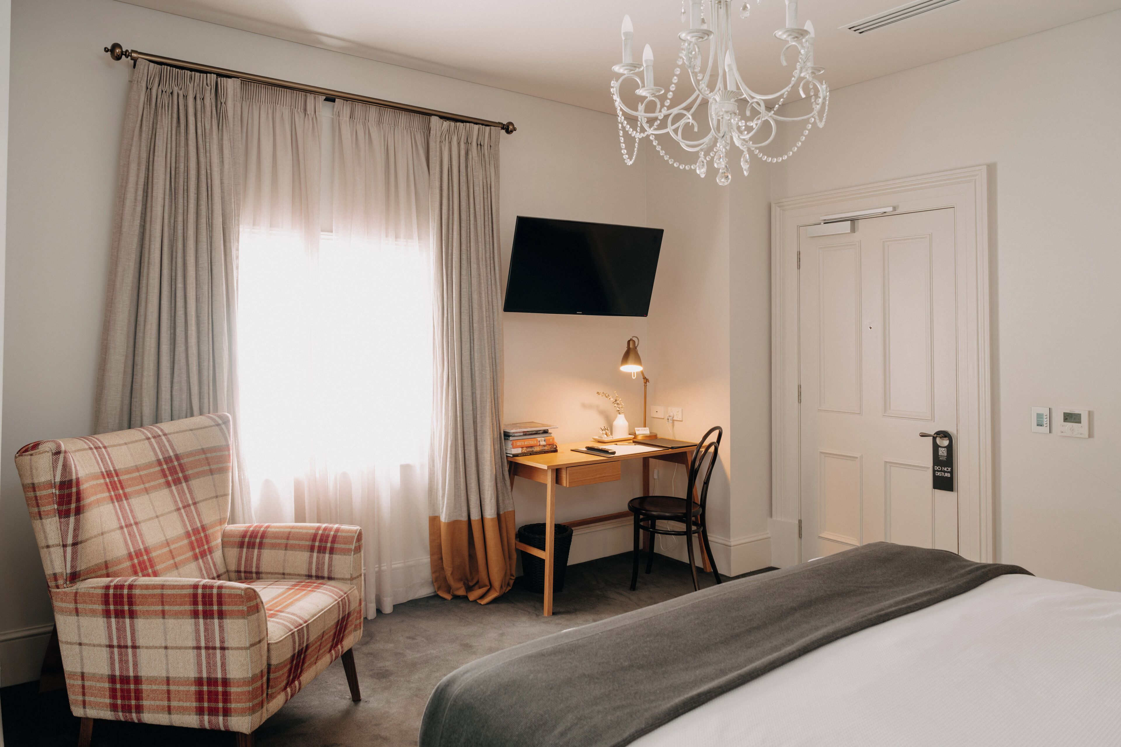 Una habitación de hotel con cama, escritorio con silla, televisor y candelabro.
