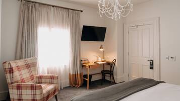 Una habitación de hotel con cama, escritorio con silla, televisor y candelabro.