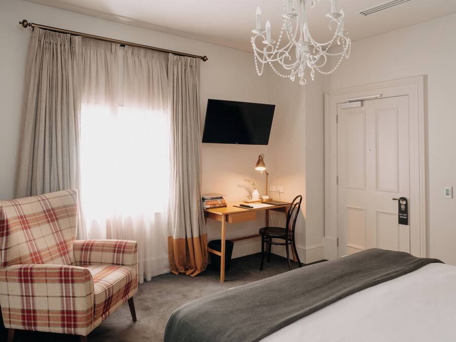 Una habitación de hotel con cama, escritorio con silla, televisor y candelabro.