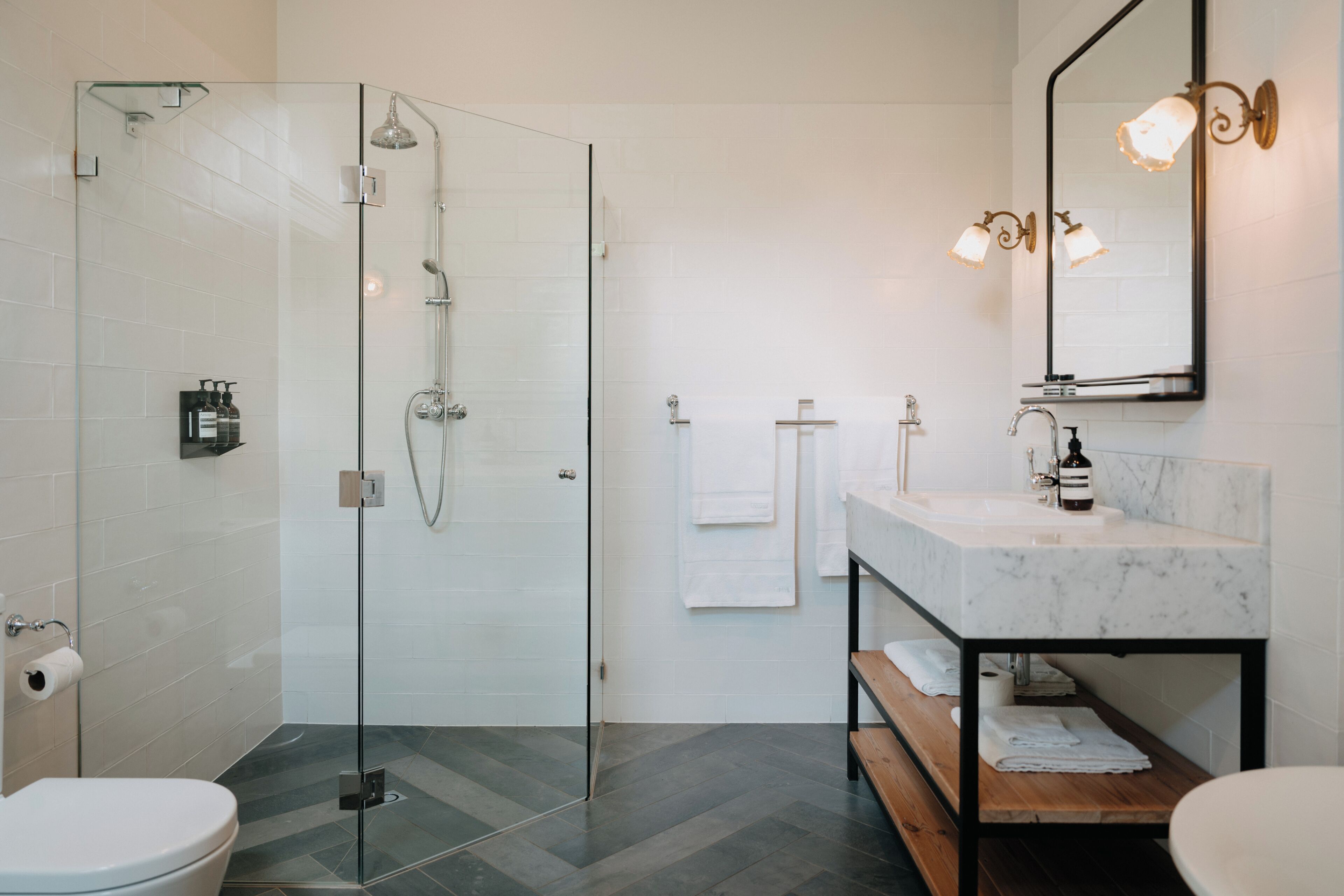 A modern bathroom with a glass-enclosed shower, a marble sink, and a wooden bench.