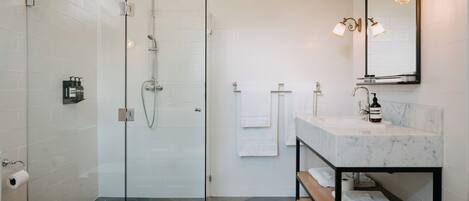 A modern bathroom with a glass-enclosed shower, a marble sink, and a wooden bench.