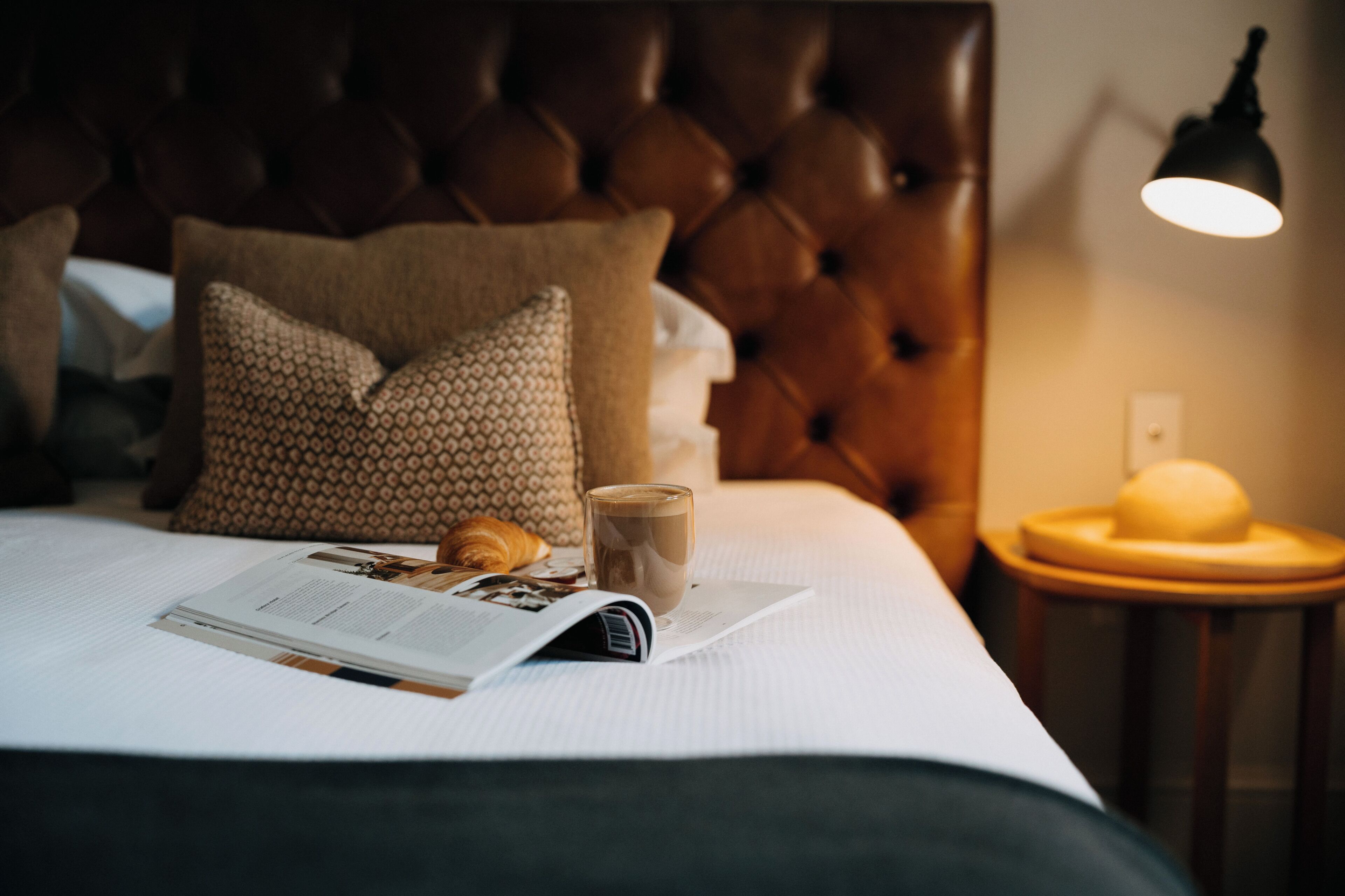 A neatly made bed with a magazine, a cup of coffee, and a croissant.