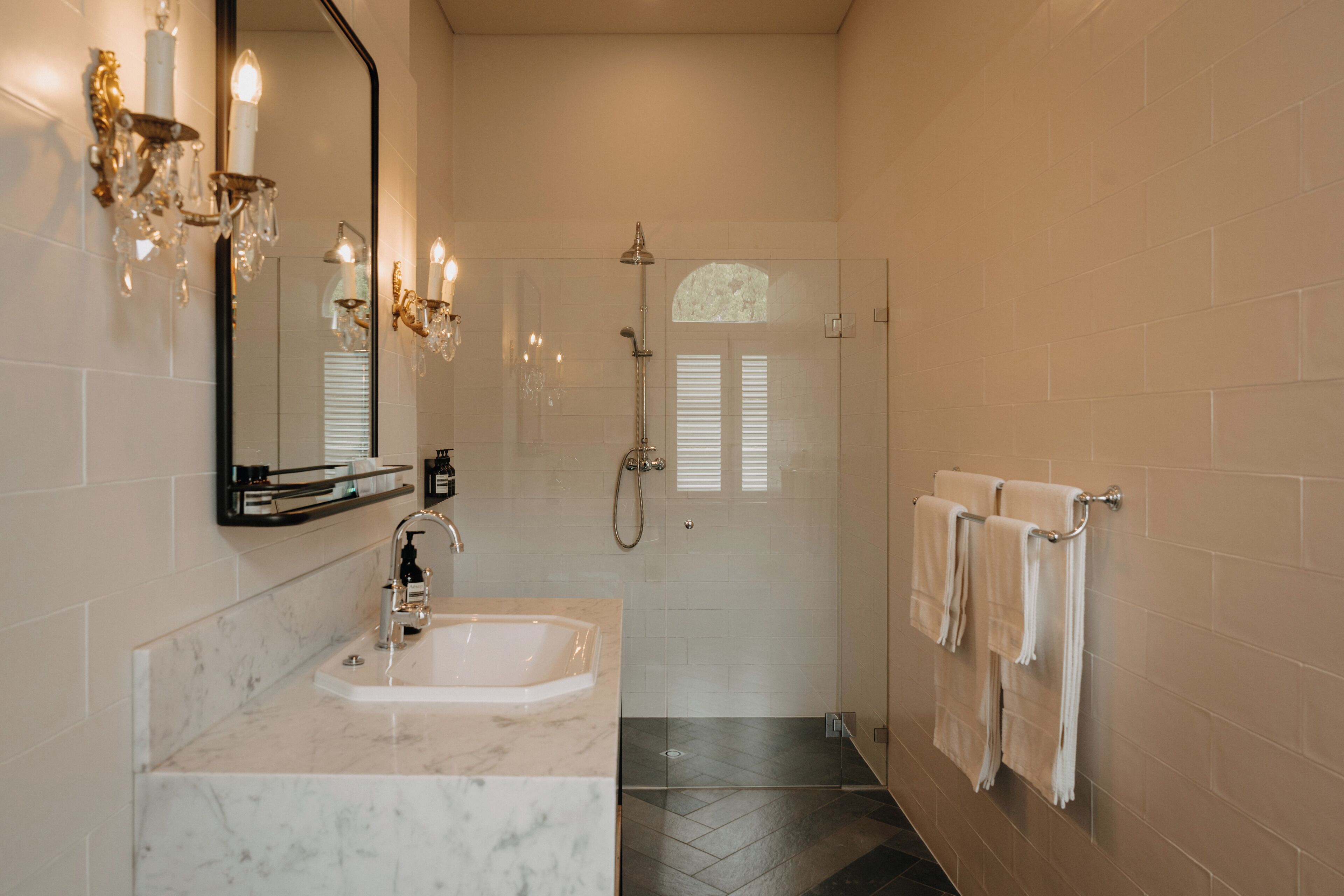 A bathroom with a marble sink, a large mirror, a chandelier, and a shower.