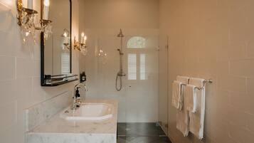 A bathroom with a marble sink, a large mirror, a chandelier, and a shower.