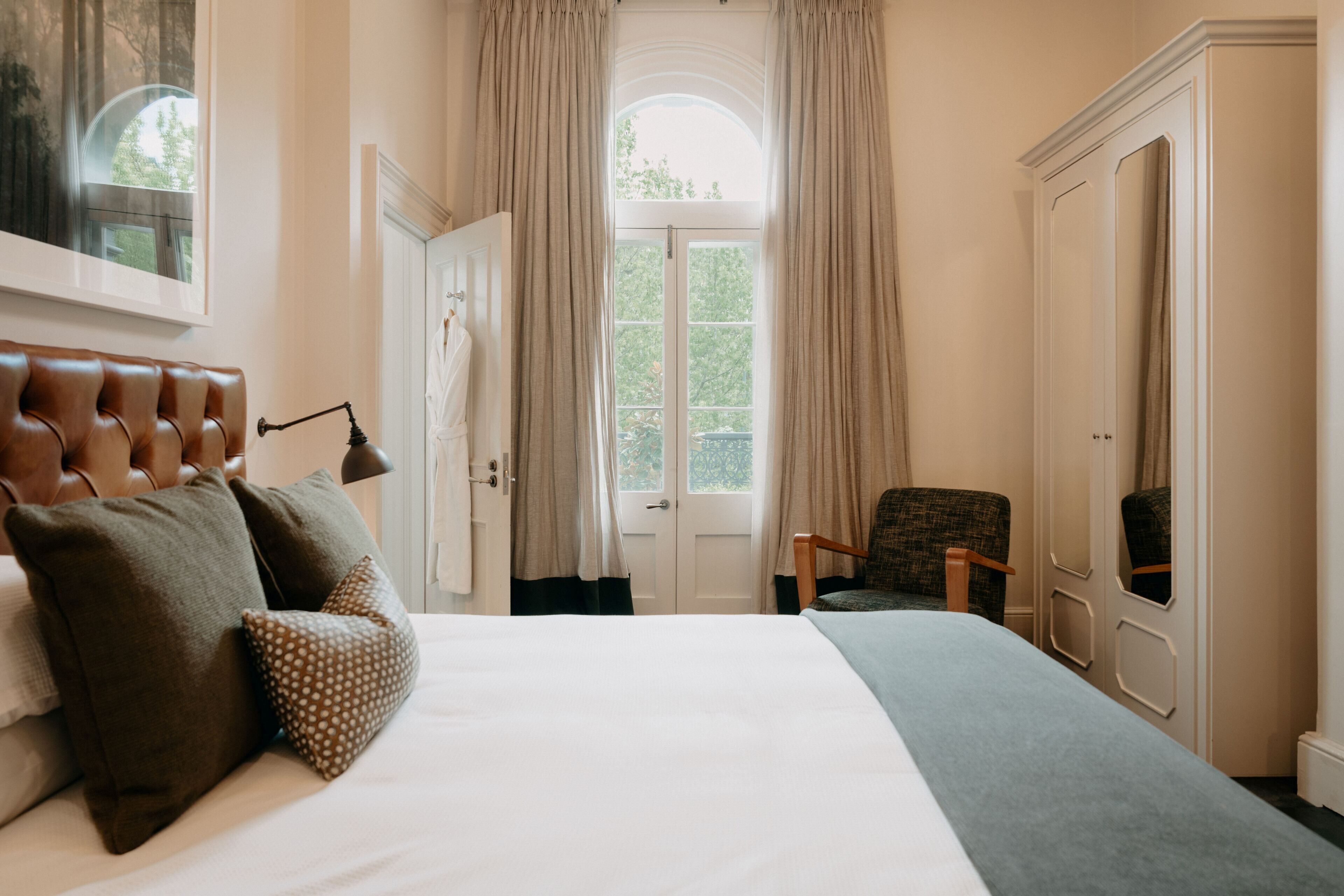 Une chambre à coucher avec un grand lit, une chaise, une armoire et une porte donnant sur un balcon.