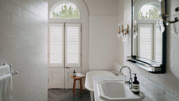 A bathroom with white brick walls, a white bathtub, a sink with a mirror, and a small wooden stool.