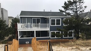 A two-story house with a balcony, a deck, and a sandy beach in the background.
