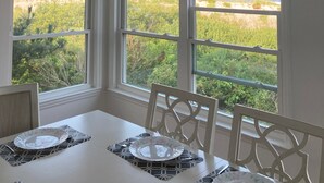 A dining room with a table set for two, large windows with a view of greenery and a distant building, and a unique ceiling light fixture made of shells.