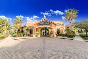 Exterior de Regal Palms, con una fachada de estilo mediterráneo, una entrada central con un letrero y palmeras circundantes.